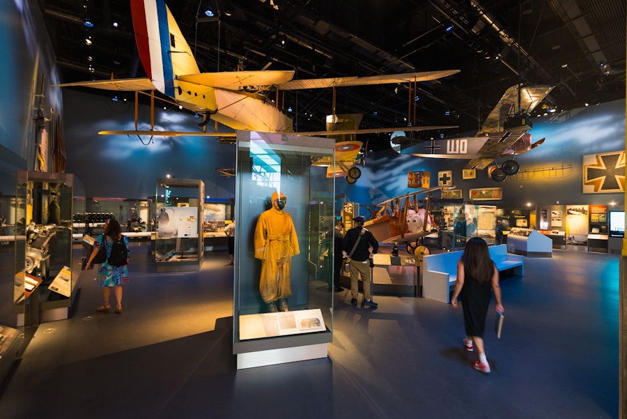 Visitors walk through an aviation exhibit with vintage aircraft and a yellow flight suit on display.