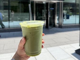 Eine Hand hält einen Matcha zum Mitnehmen hoch.
