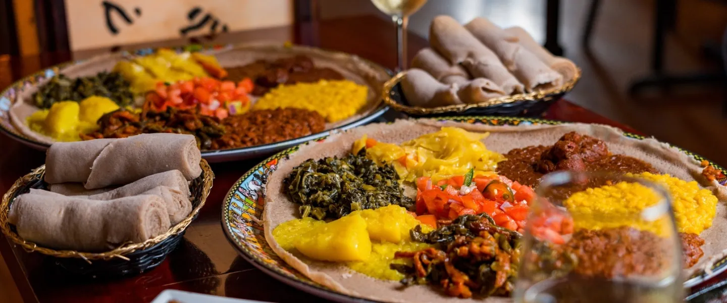 Platters of colorful Ethiopian dishes with injera bread, lentils, greens and stews arranged on a table.