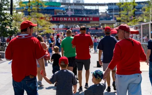 Families in red jerseys walking toward Nationals Park for a baseball game.
