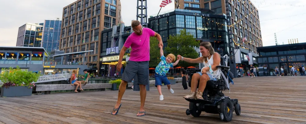 Parents hold their child's hands and swing him in the air as they enjoy a day on the Wharf. 