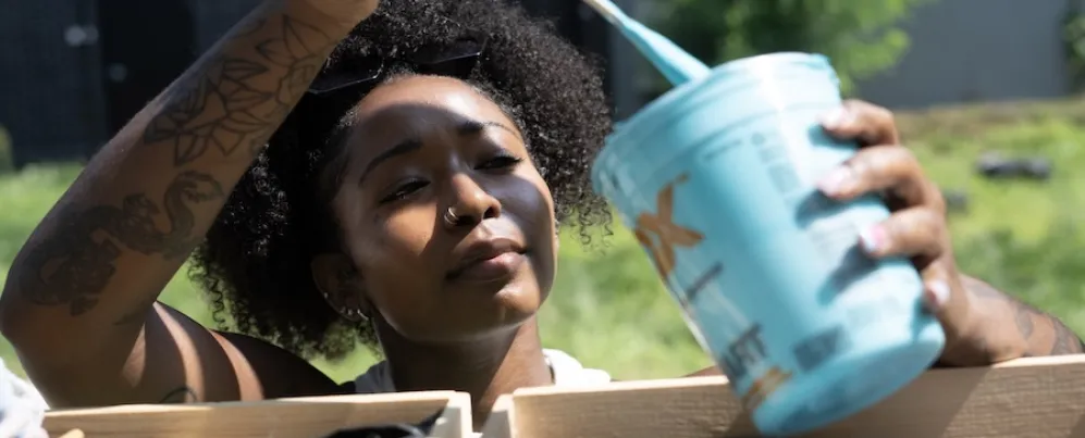 An artist dips a brush into a container of brightly colored paint.