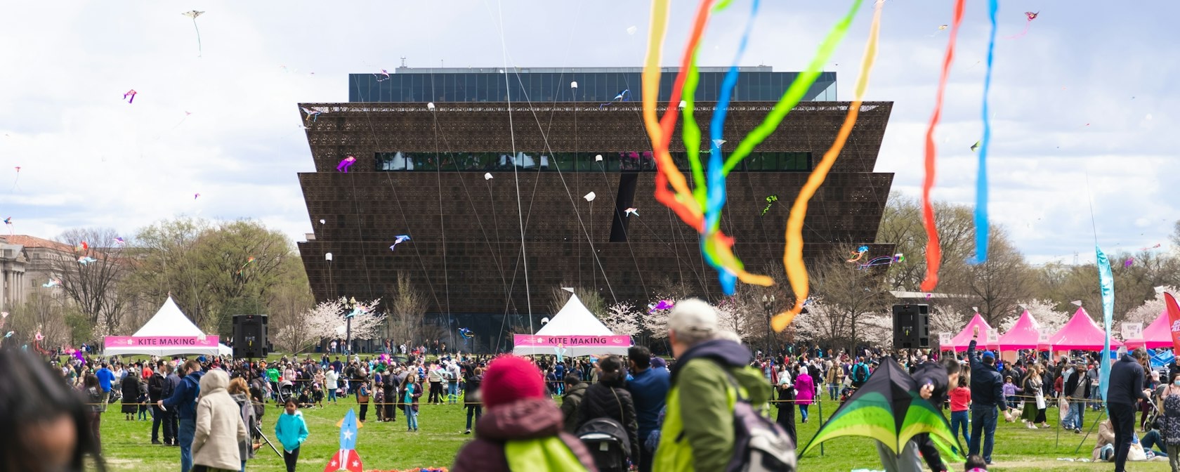 Une scène colorée du Blossom Kite Festival avec des cerfs-volants volant dans le ciel devant le Musée national d'histoire et de culture afro-américaines.