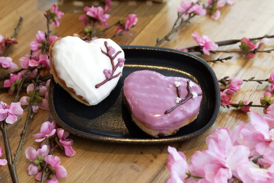 Deux beignets en forme de cœur décorés de branches de fleurs de cerisier sont posés sur une table ornée de fleurs de cerisier.
