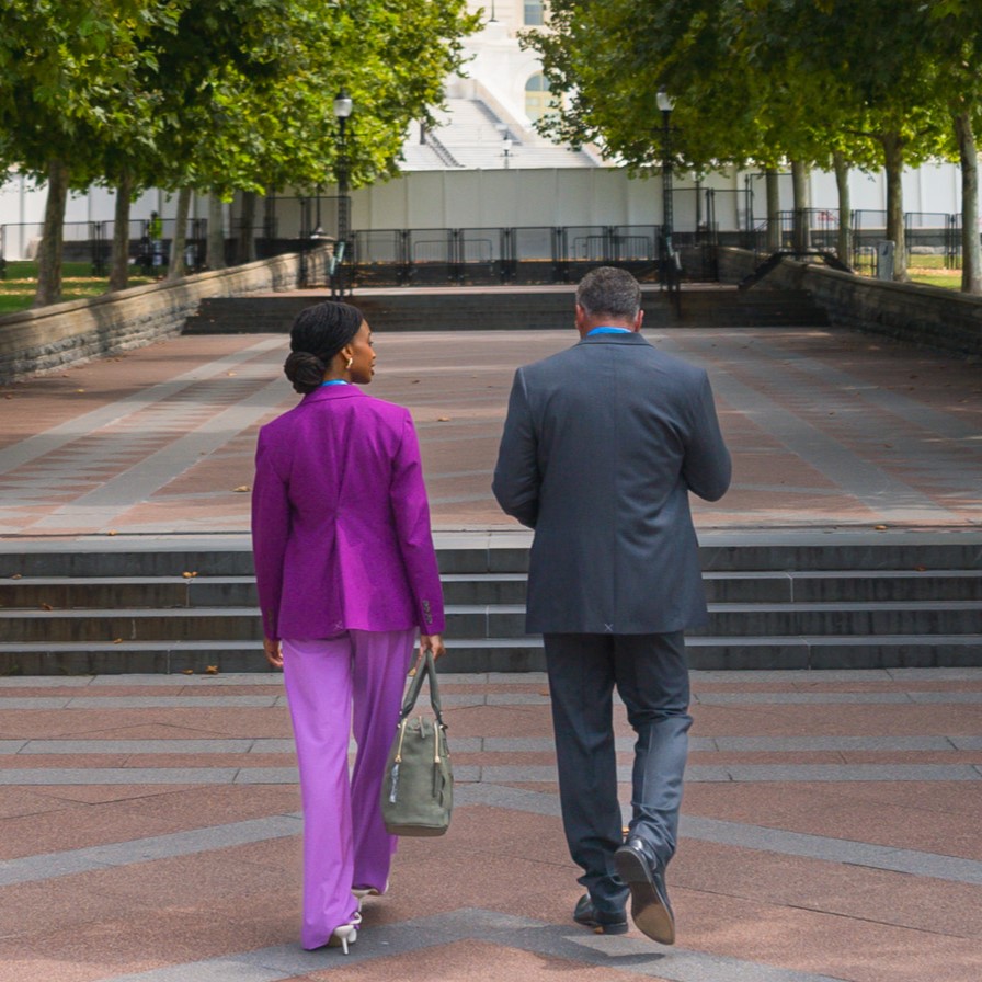 Dos personas caminando por una acera de ladrillos rodeada de árboles verdes.