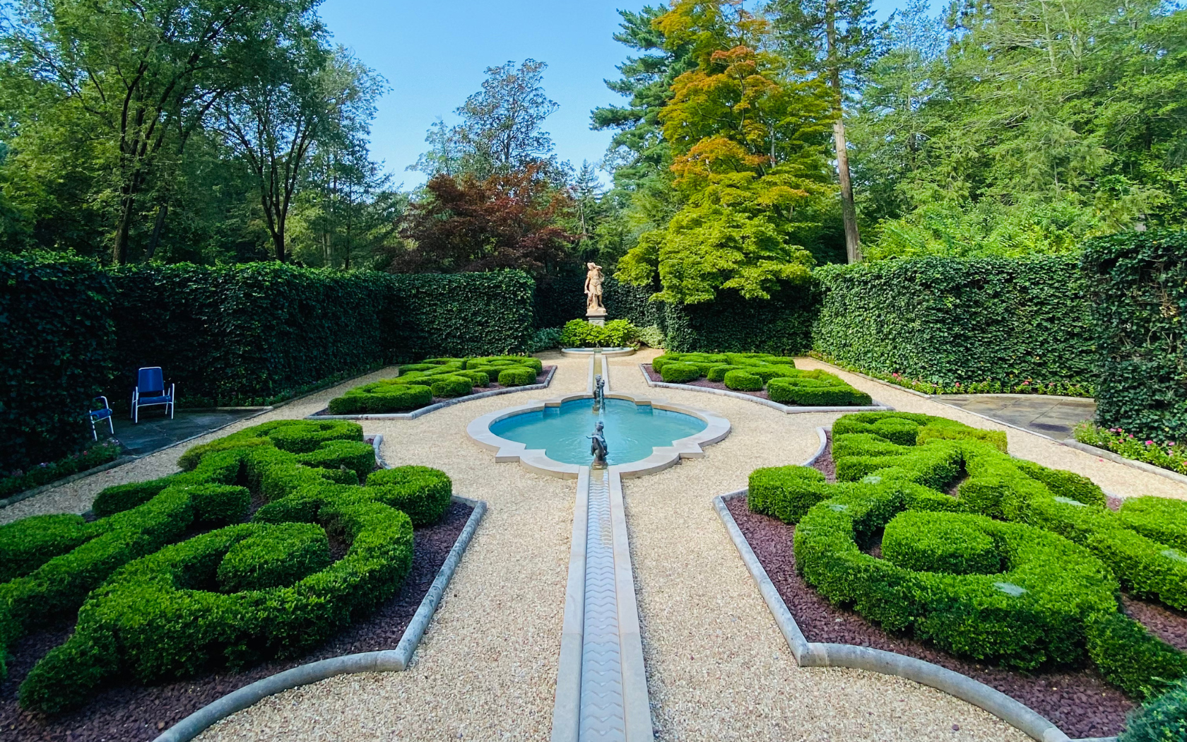 Jardin formel avec des haies de buis sculptées, une fontaine centrale et une statue classique entourée de hautes haies vertes à Washington, DC.
