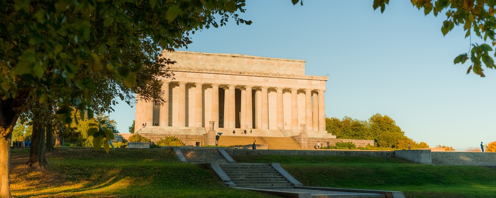 The Lincoln Memorial at sunset framed by trees with golden light on the monument’s columns.