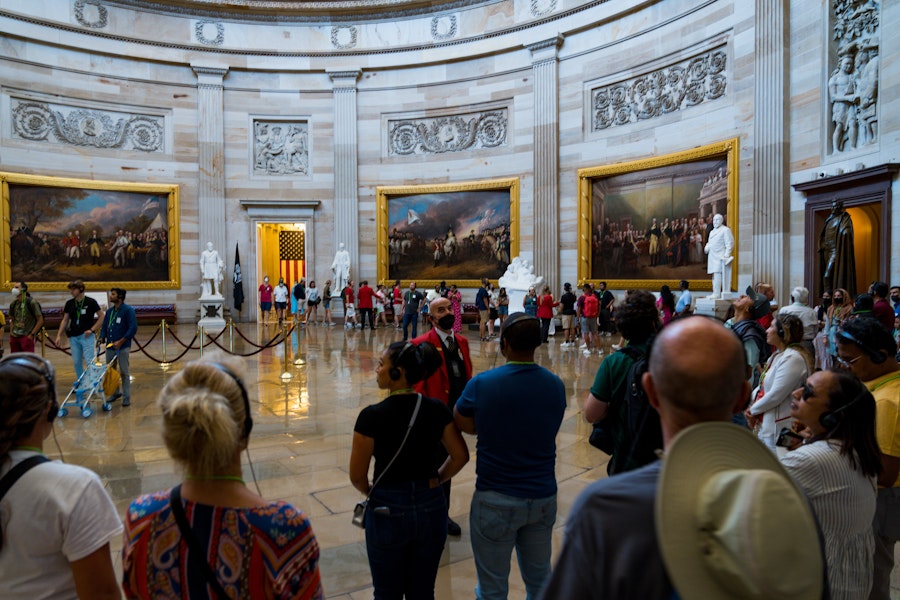 Visitors gather inside the U.S. Capitol Rotunda surrounded by large historic paintings and statues.