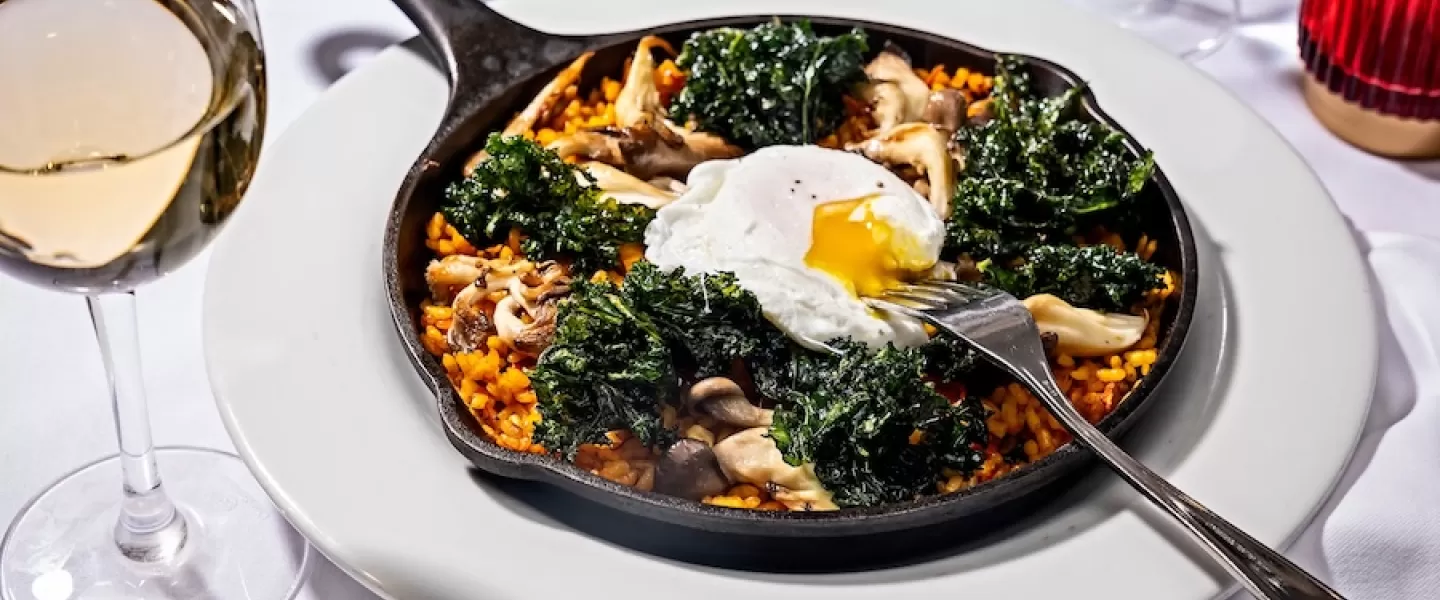 skillet with paella, kale and fresh egg on a white table spread